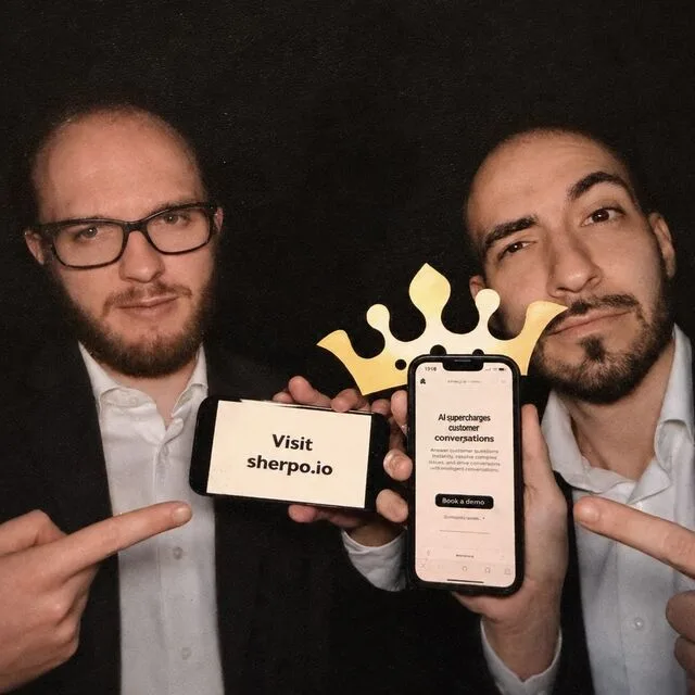Sherpo's founders in a photo booth, pointing at phones showing sherpo.io.